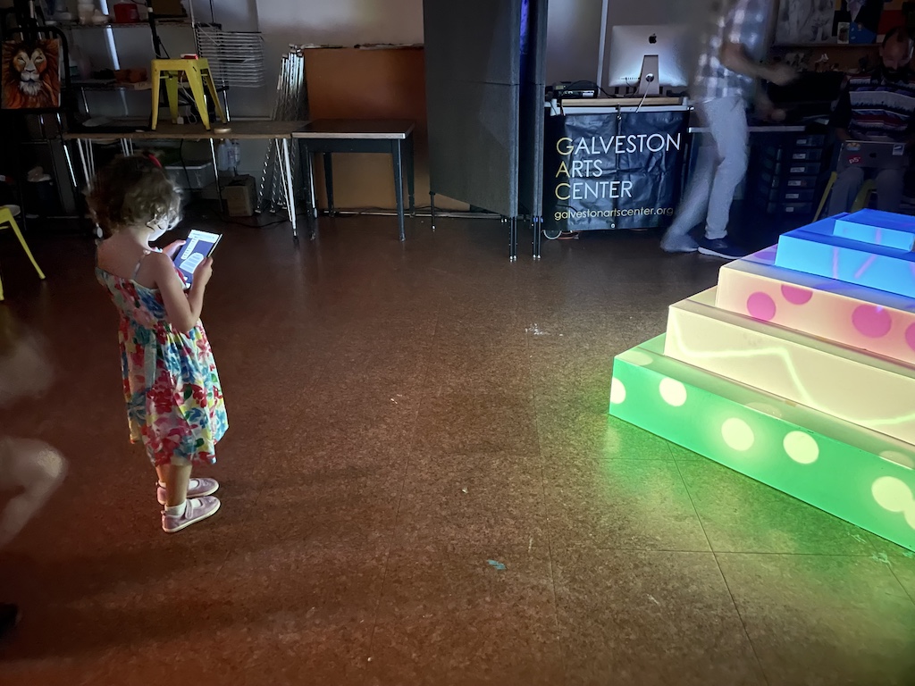 A child uses a table to paint on the image of a sculpture. Nearby, the drawing is projected onto the surface of the real sculpture.